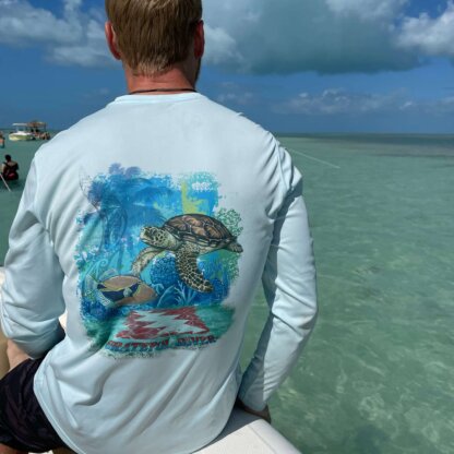 A man sitting on a boat with a Grateful Diver Aloha Turtle UV Shirt on the back of his shirt.