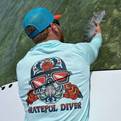 A man on a boat holding a fish in his hand while wearing the Grateful Diver Sugar Skull UPF 50+ Hoodie.