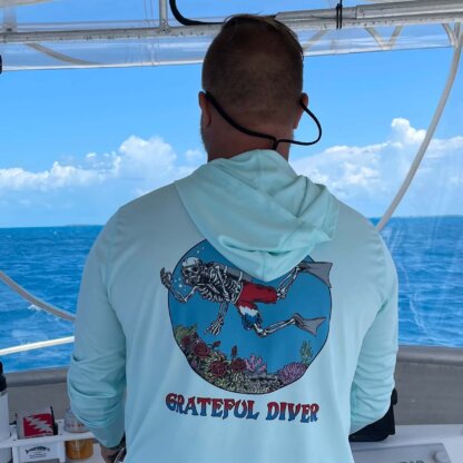 A man on a boat wearing a Grateful Diver Skeleton Diver UPF 50+ Hoodie that says grateful dive.