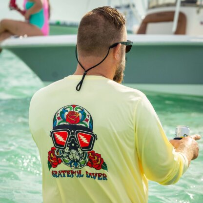 A man wearing yellow sunglasses and a Grateful Diver Sugar Skull UV Shirt is standing in the water.