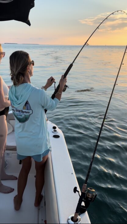 Two women wearing Salty Soul Charters UPF 50+ Hoodies fishing on a boat at sunset.